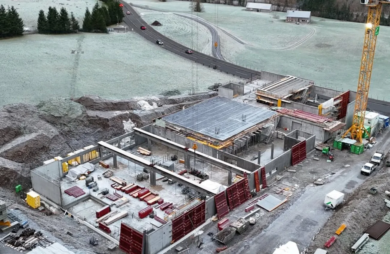 Neubau der Briganto Unternehmenszentrale in Andelsbuch, Vorarlberg. Luftaufnahme zeigt den aktuellen Stand der Betonarbeiten und die Einbettung des Firmengeländes in die Region.
