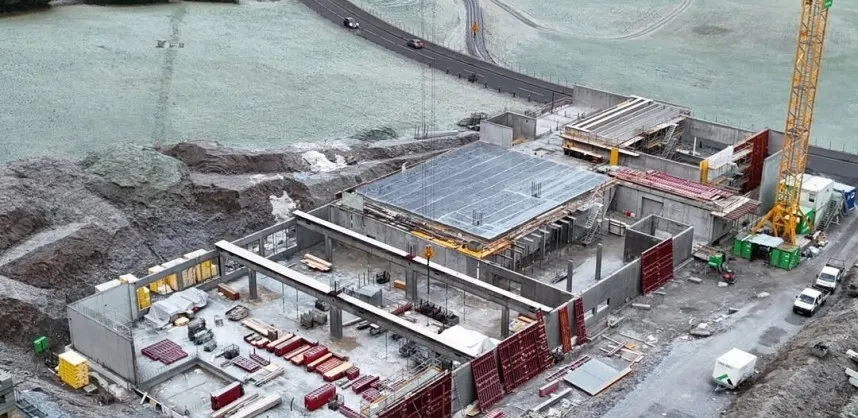 Neubau der Briganto Unternehmenszentrale in Andelsbuch, Vorarlberg. Luftaufnahme zeigt den aktuellen Stand der Betonarbeiten und die Einbettung des Firmengeländes in die Region.